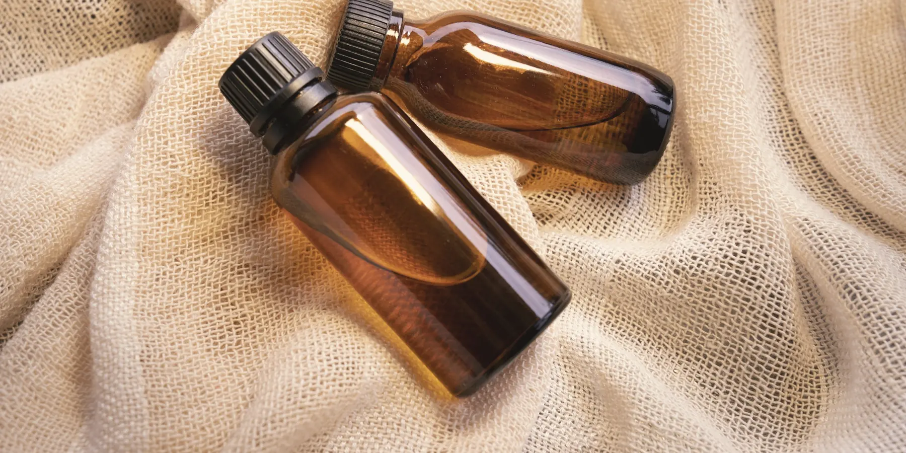 Two amber bottles of massage oil resting on cream linen
